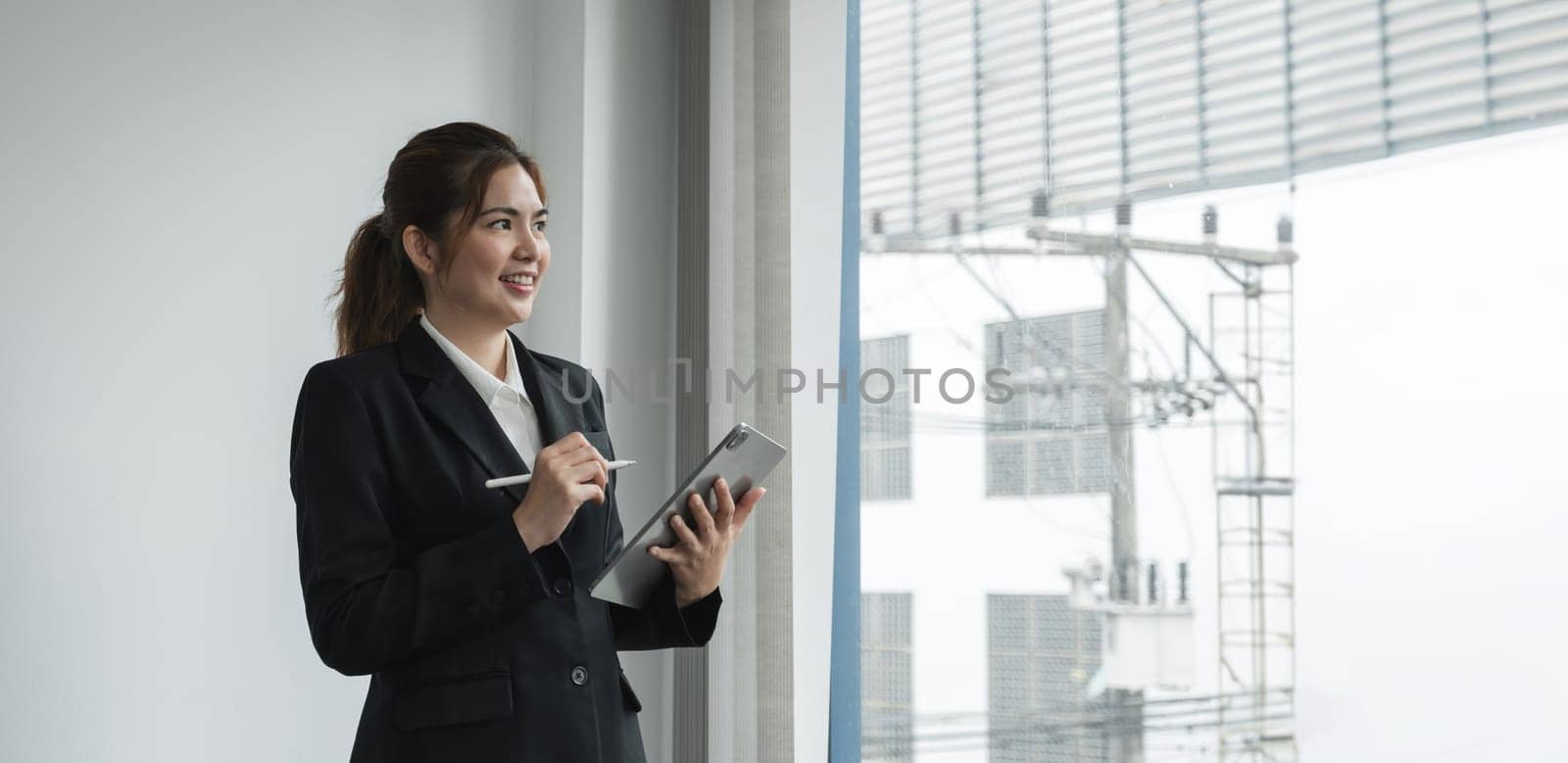 Young asian businesswoman using the tablet to analyze business data while she is standing at the office. by wichayada