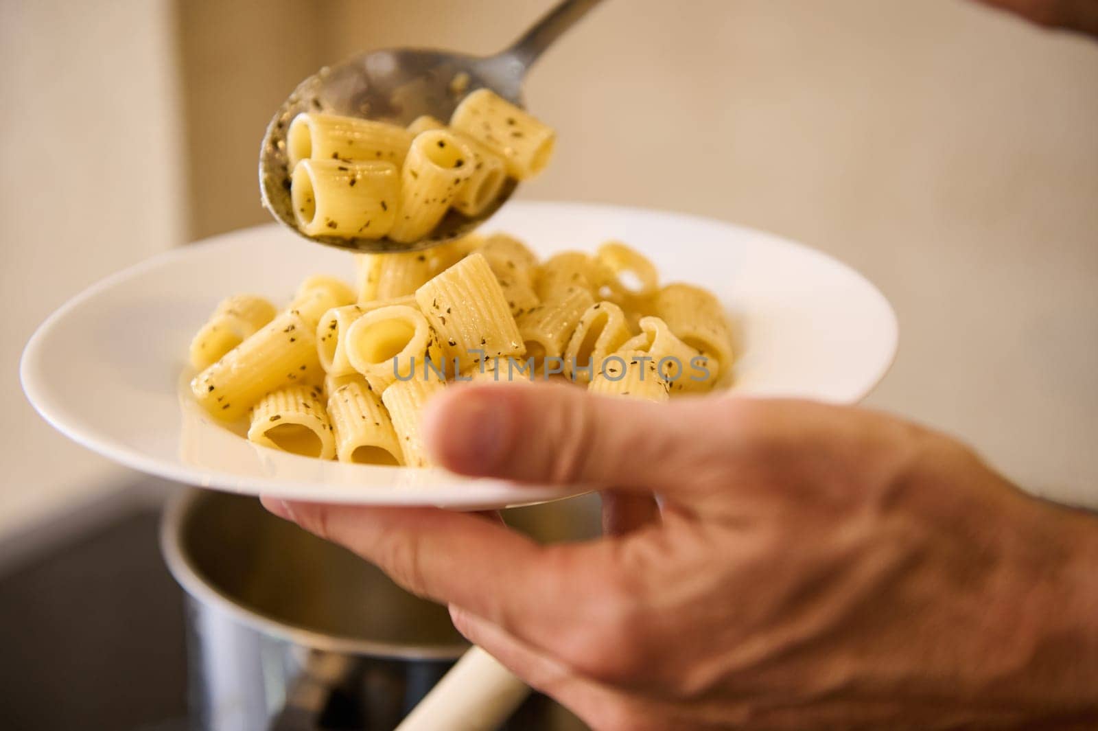 Close-up pouring Italian pasta on white plate before plating up and serving to the customers by artgf