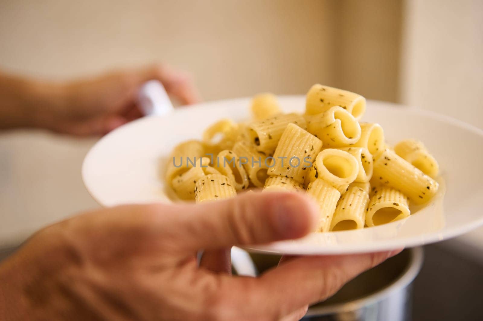 Close-up pouring Italian pasta on white plate before plating up and serving to the customers. Chef holds plate with freshly cooked Italian pasta. Food background