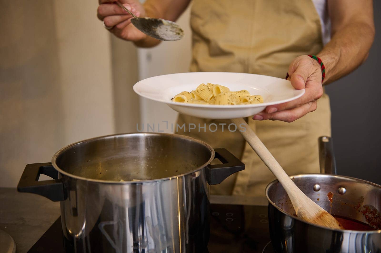 Close-up male chef standing at electric stove and putting freshly cooked pasta on a white plate