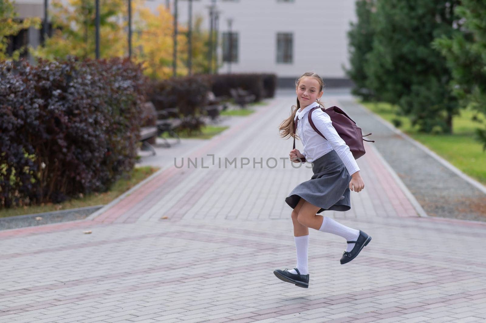 Happy caucasian girl in uniform and with a backpack jumping outdoors after school. by mrwed54