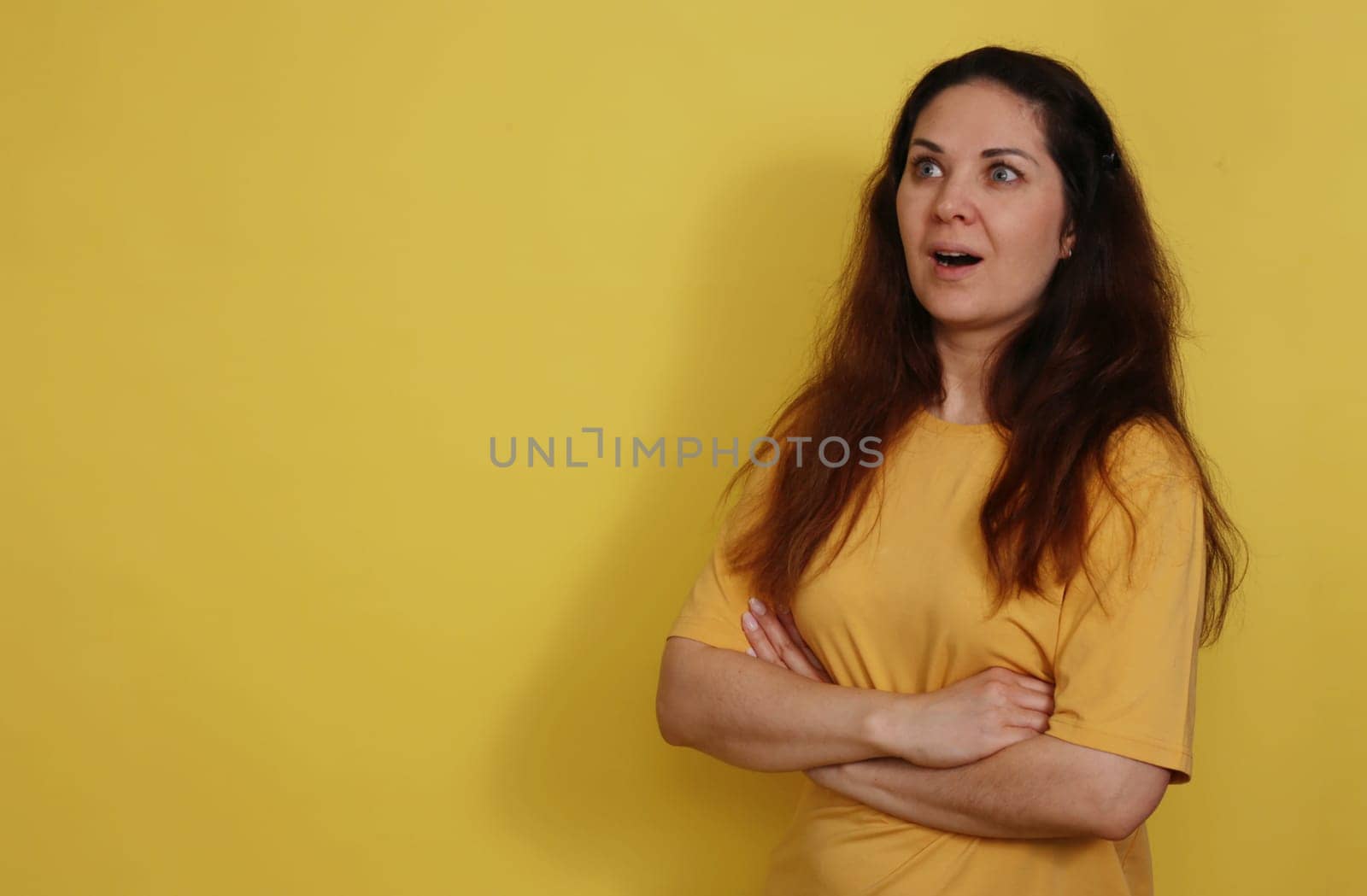 Beautiful woman in yellow T-shirt with long dark hair opened her mouth in surprise. Portrait of a surprised beautiful woman with the expectation of darkness in a yellow tank top on a yellow background.