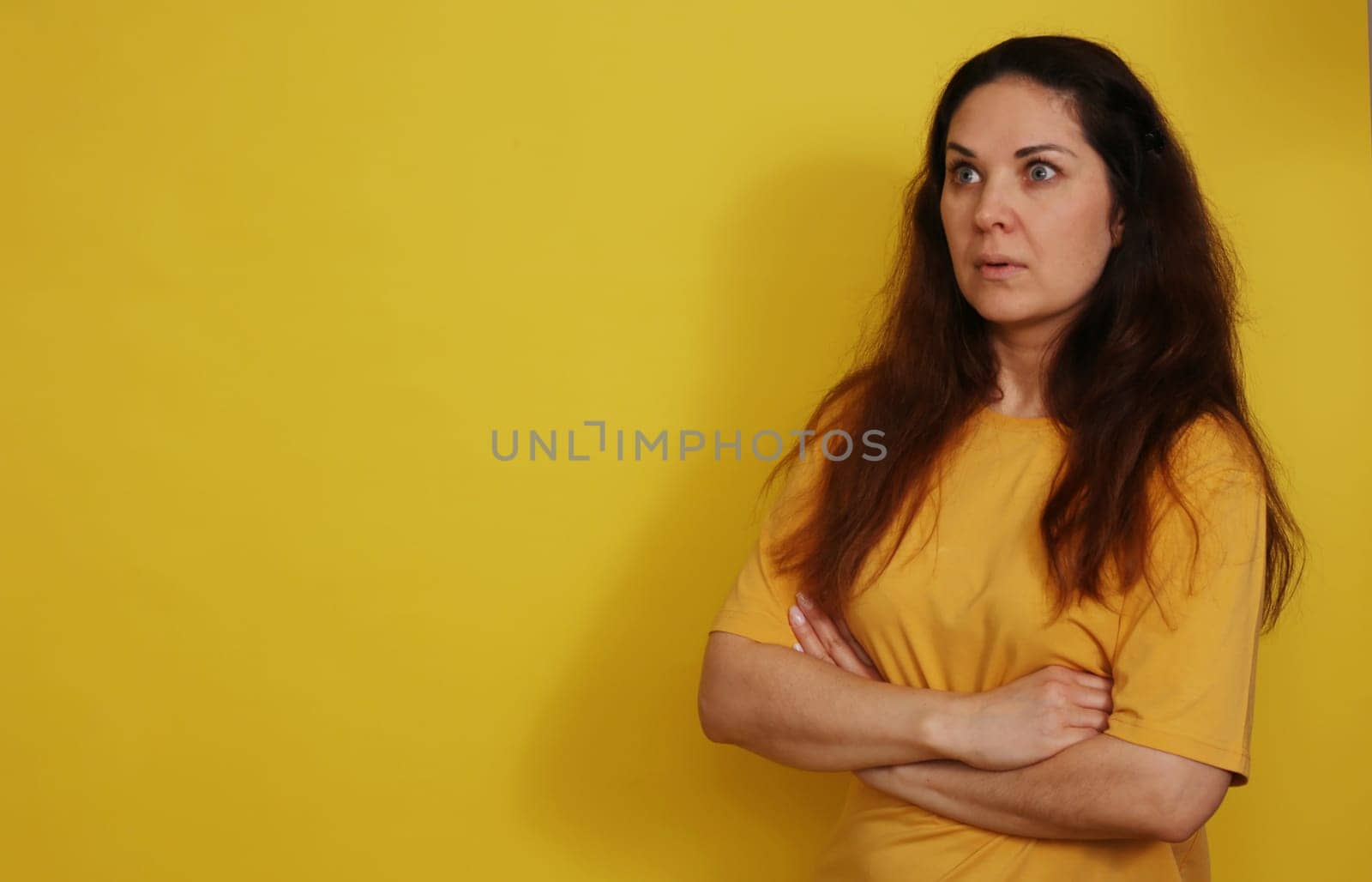 A beautiful woman in a yellow T-shirt with long hair in a state of bewildered surprise. Woman posing with her arms crossed.