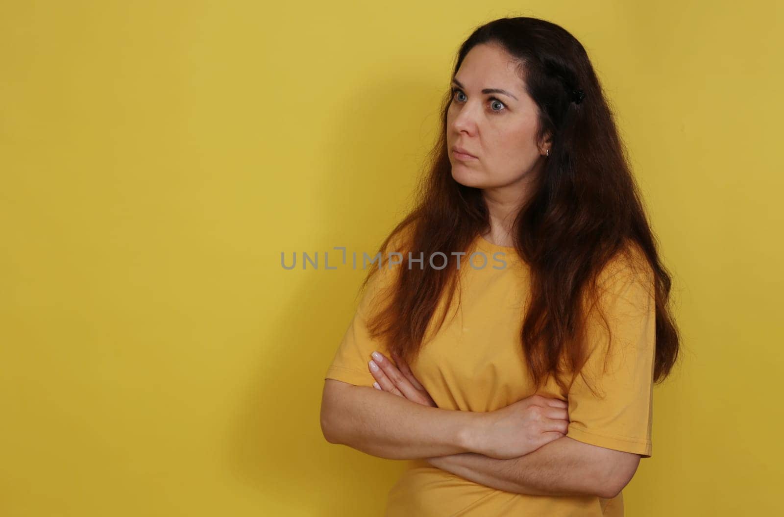 Beautiful woman in yellow t-shirt on yellow studio background with long dark hair. Portrait of a surprised beautiful woman.