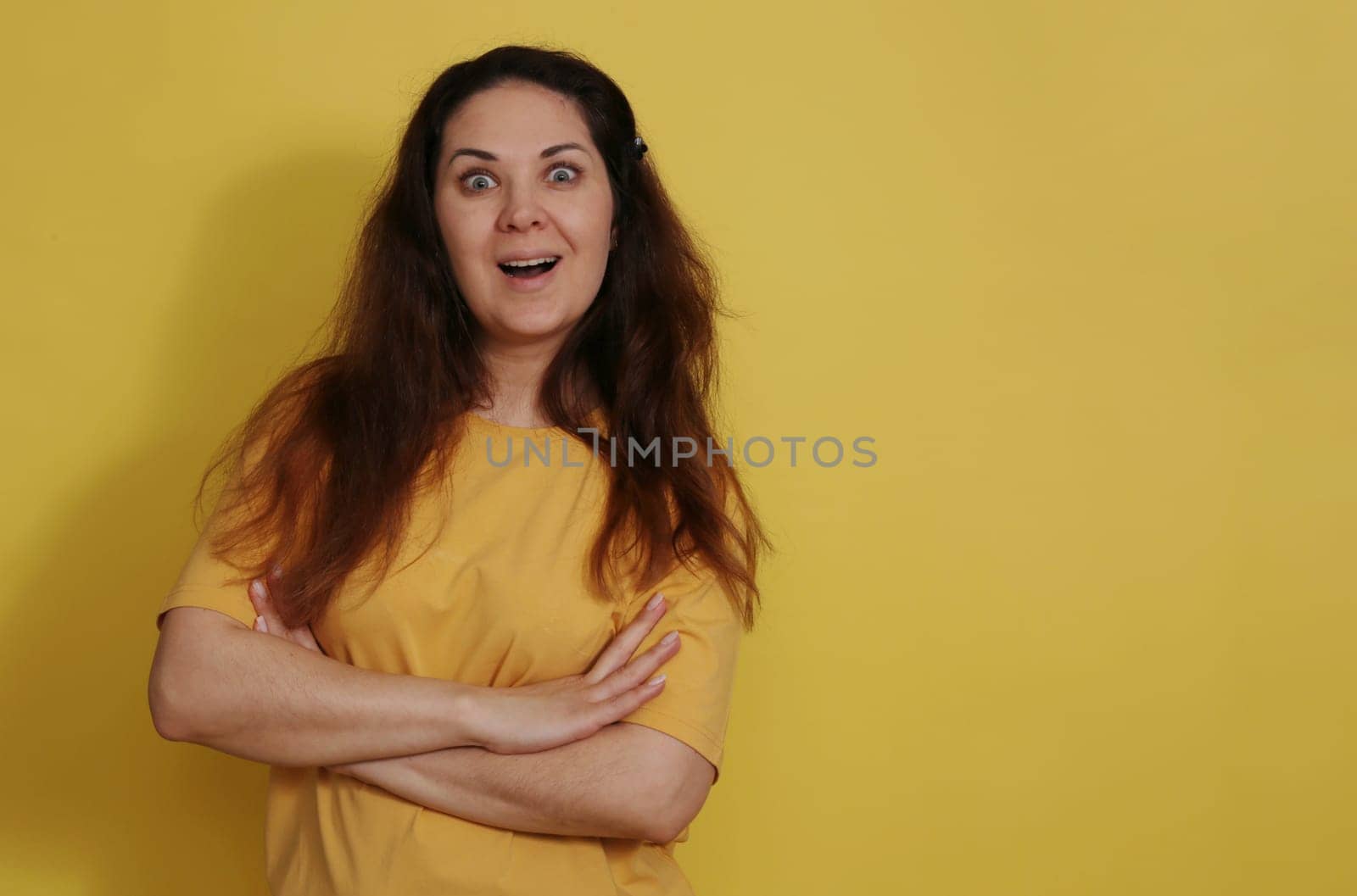 Close-up portrait of a charming surprised woman in a cotton t-shirt, good reaction to the news. The reaction of a woman in a yellow T-shirt on a yellow background received a pleasant unexpected news.