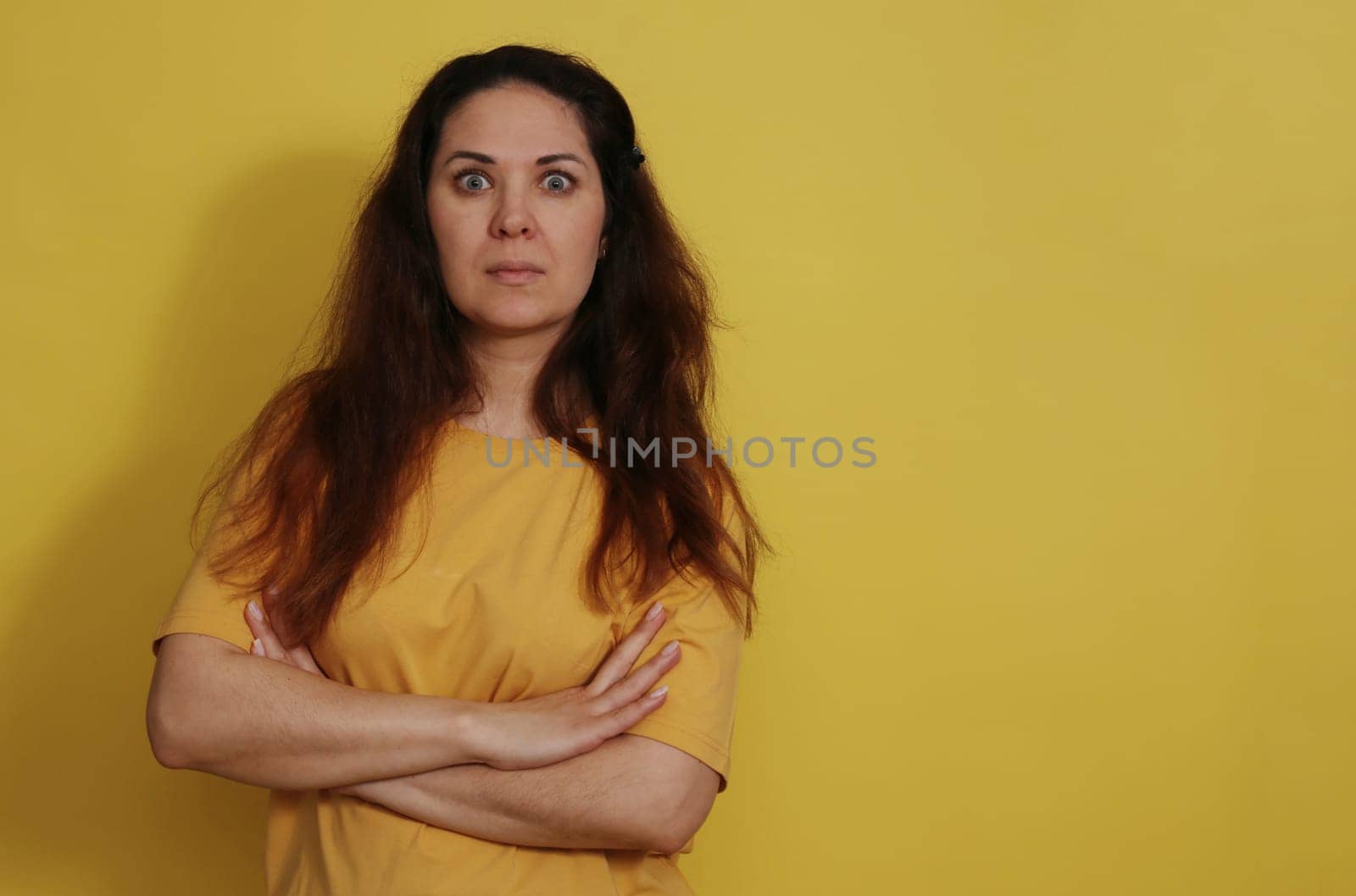 The beautiful brunette woman goggled her eyes out in surprise. Portrait of a surprised beautiful woman with the expectation of darkness in a yellow tank top on a yellow background.