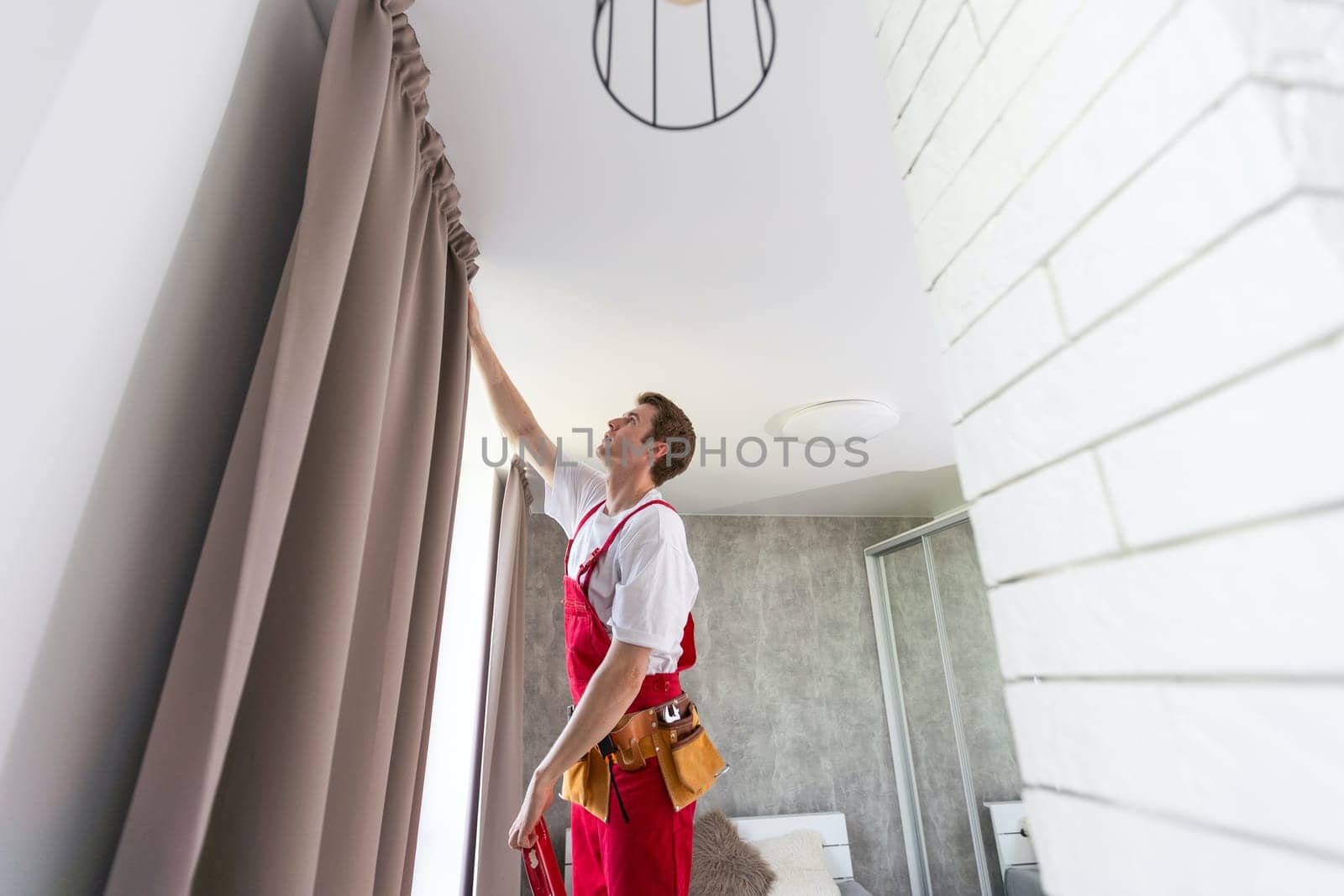 worker installing window curtain rod on the wall by Andelov13