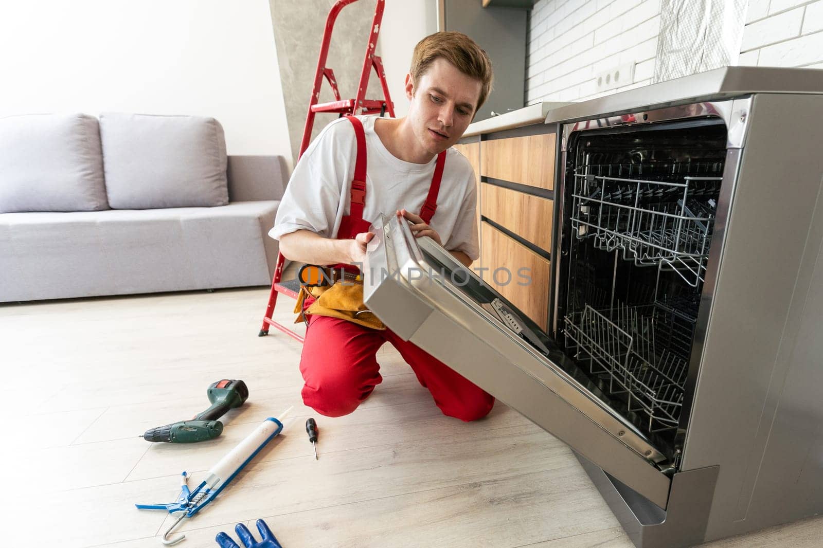 Repairman checks operating state of dishwasher in kitchen.