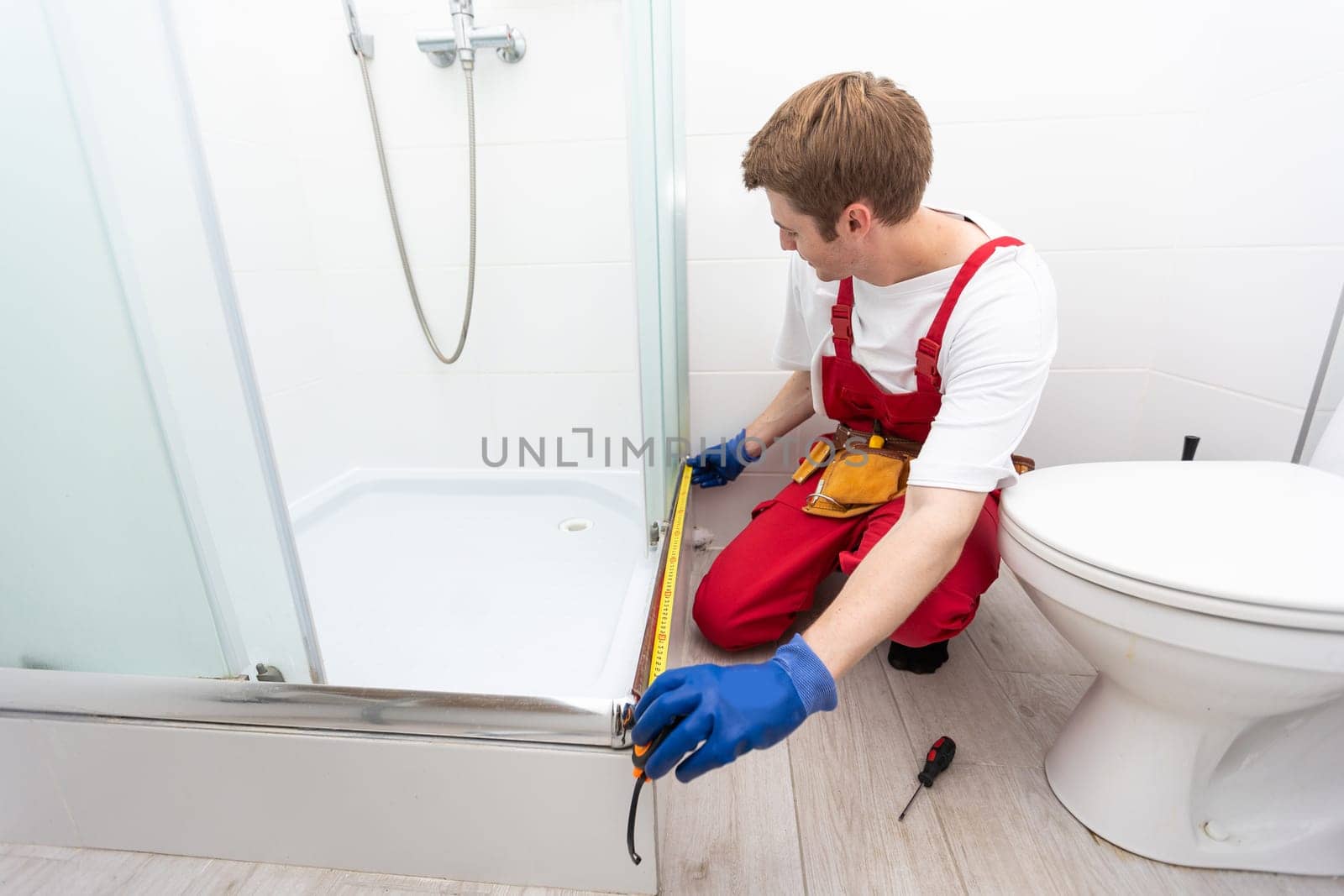 repairmen in uniform measuring modern shower cabin in bathroom by Andelov13