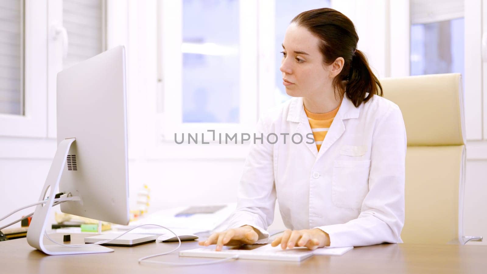 Female doctor typing using computer in a clinic by ivanmoreno