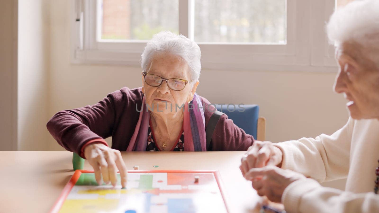 Two old friends playing Parcheesi board game in a nursing home
