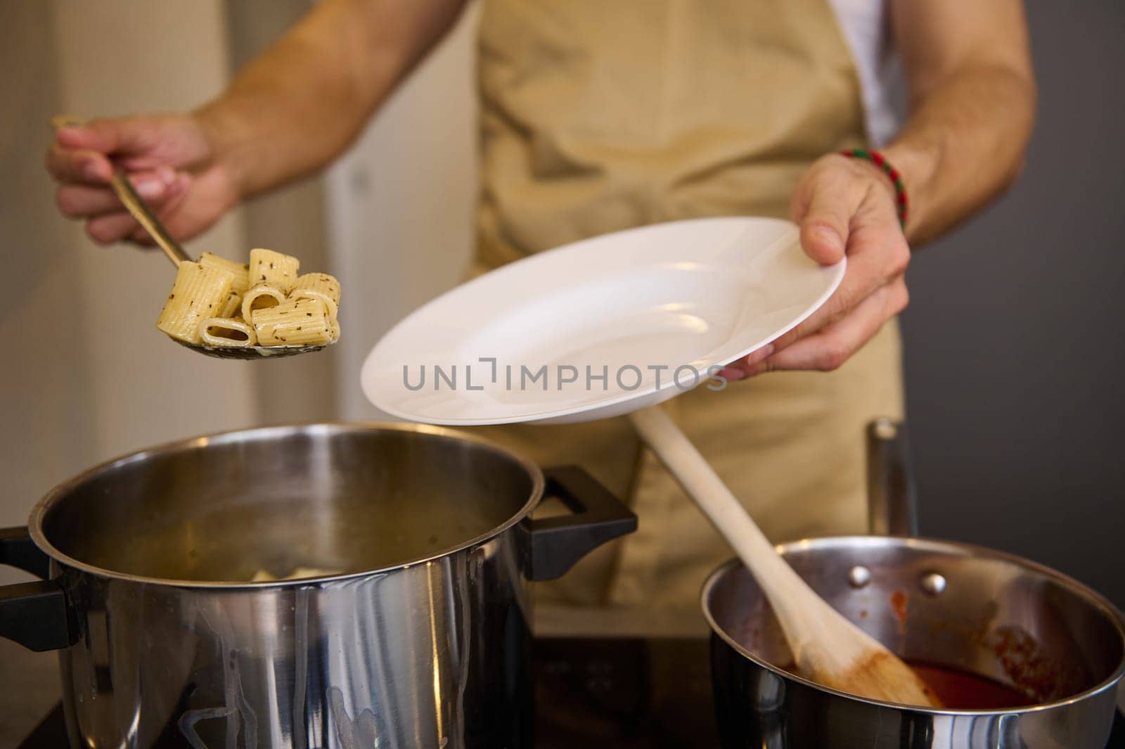 Close-up male chef standing at stove and putting freshly cooked pasta penne on a white plate by artgf