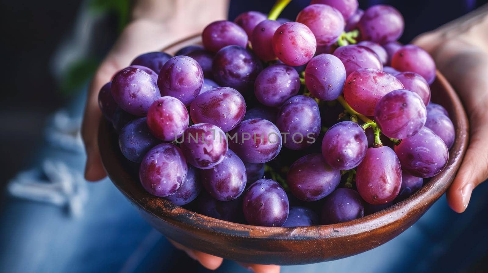 A person holding a bowl of purple grapes in their hands