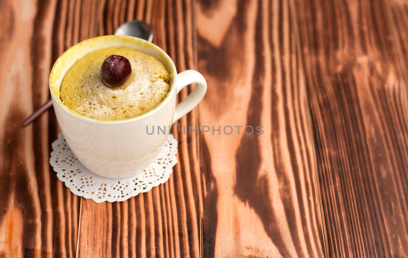 muffin in a mug, cooked in the microwave. The cupcake is decorated with a cherry. Homemade cakes in a mug. Vanilla dessert with cherry on top. High quality photo