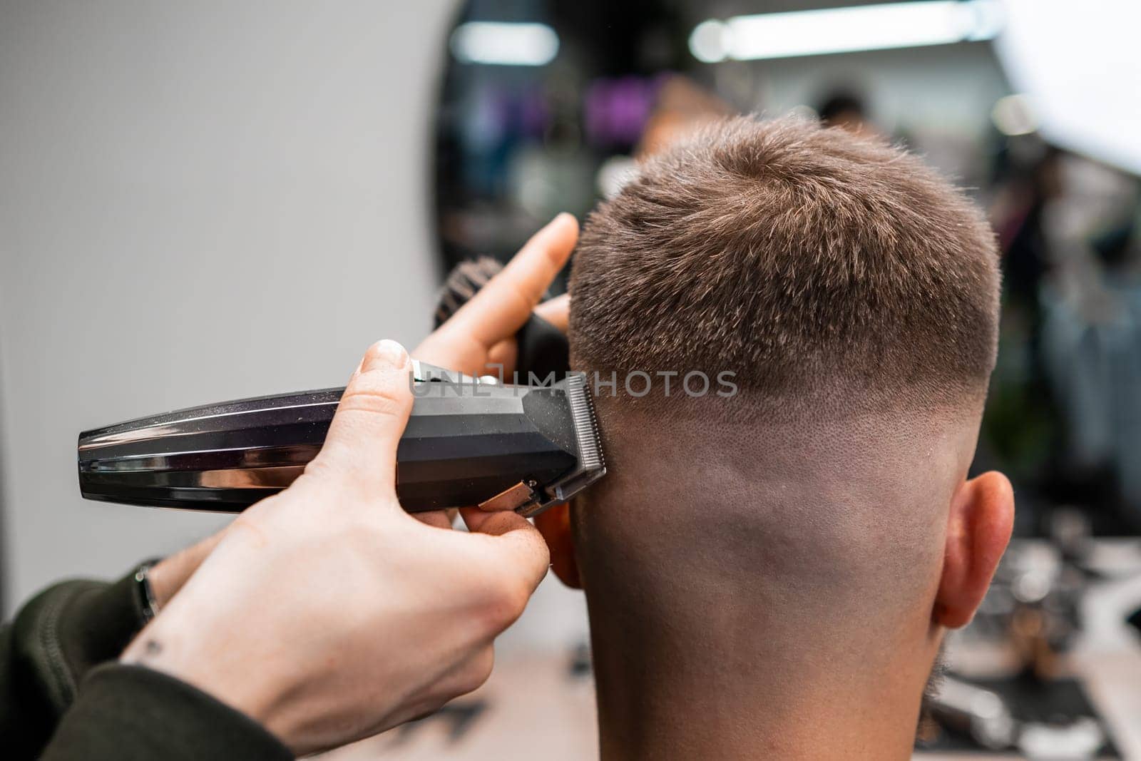 Barber cuts client short hair with trimmer in barbershop by vladimka