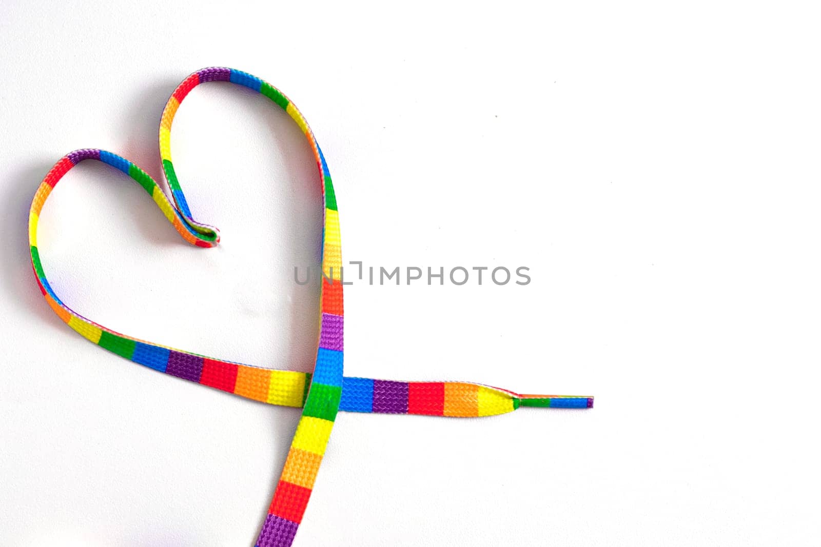 A colorful gay flag ribbon lies in the shape of a heart on a white background. LGBT rainbow ribbon pride ribbon symbol. Same-sex love and wedding concept. month or happy singles day. Gay pride