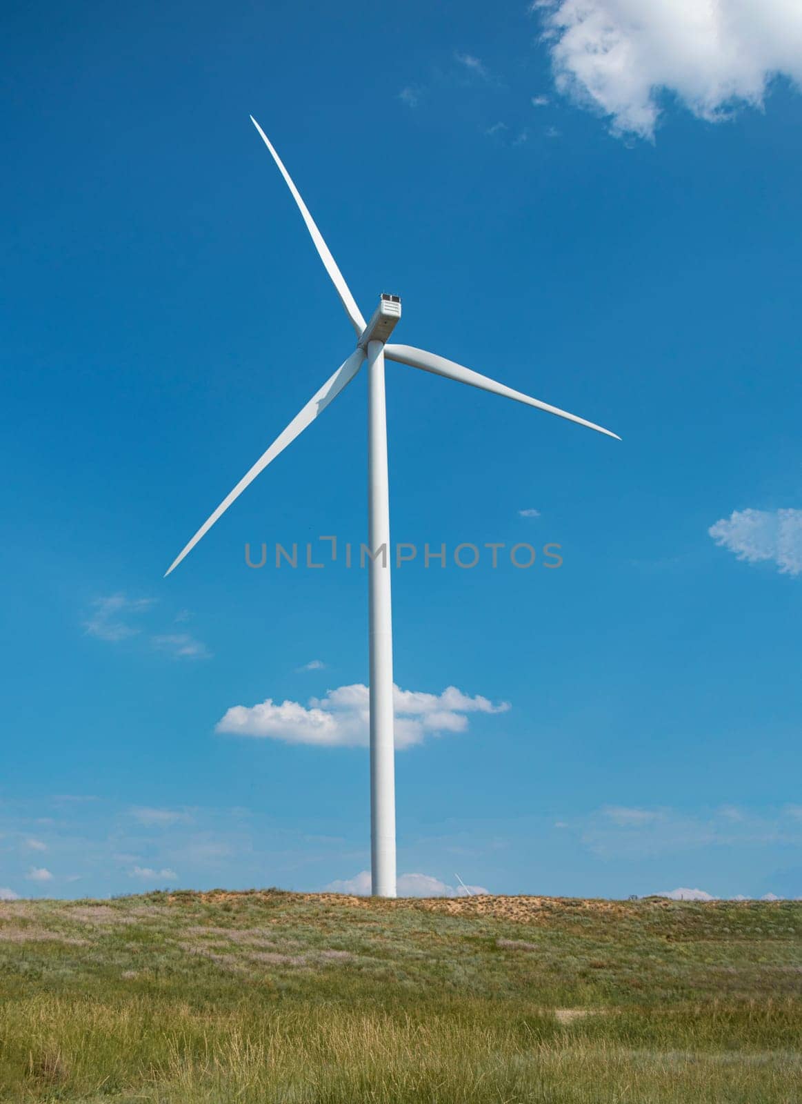 windmill on the background of the cloudy blue sky. Concept of alternative energy production from wind. Modern windmill with full-length blades. High quality photo