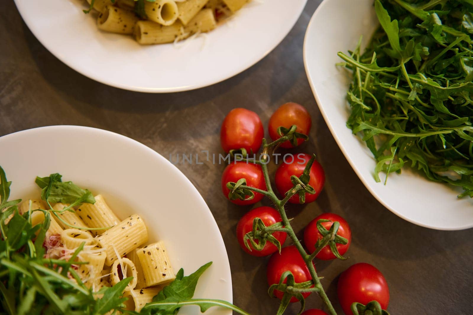 Food background with a branch of fresh ripe organic tomatoes cherry near plates of Italian pasta penne a la Amatriciana with pancetta bacon and pecorino cheese. Italian cuisine and culture. by artgf