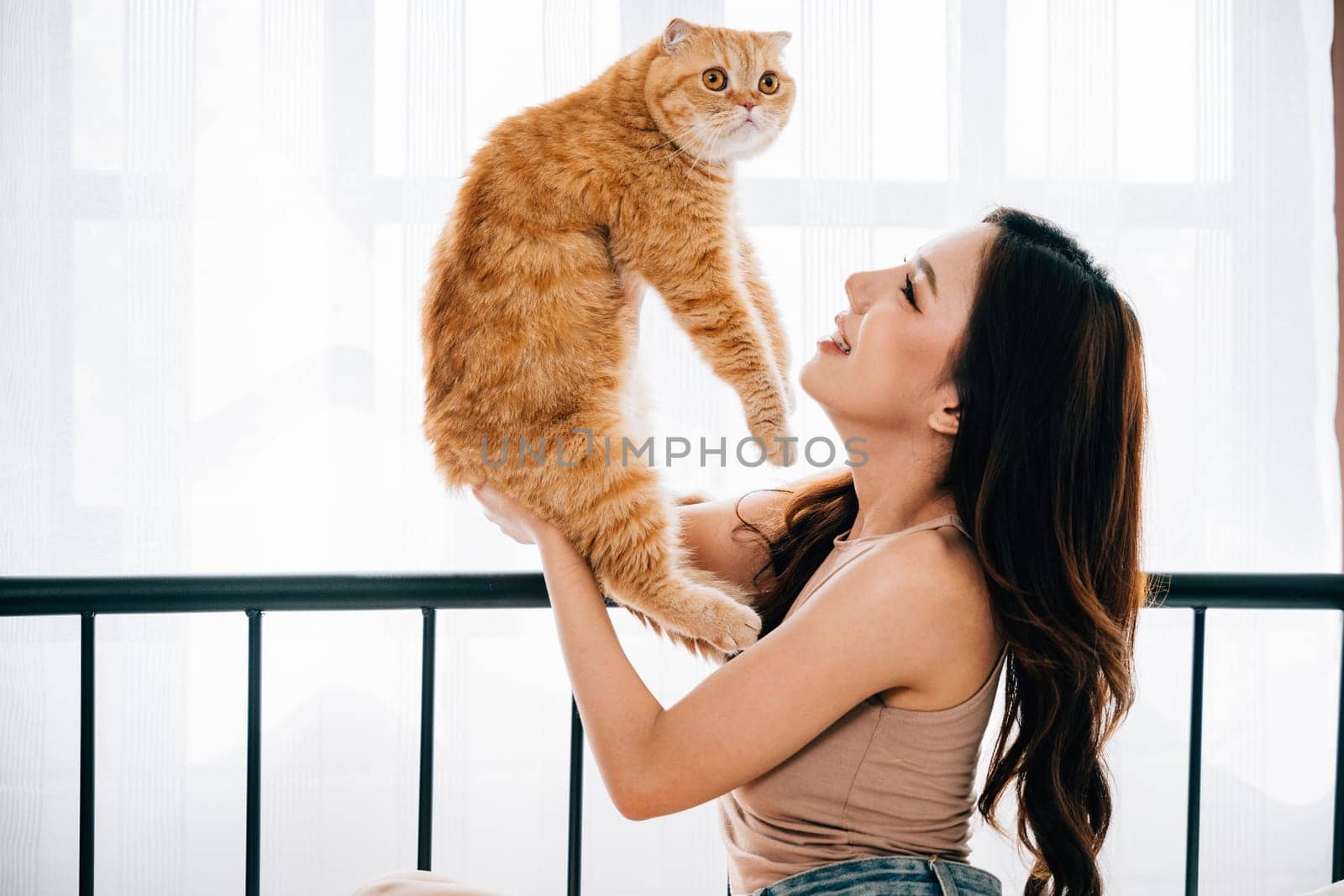 In a cozy bedroom, a beautiful woman shares an affectionate hug with her playful Scottish Fold cat, radiating happiness and support. Their bond is heartwarming and delightful. Pet love by Sorapop