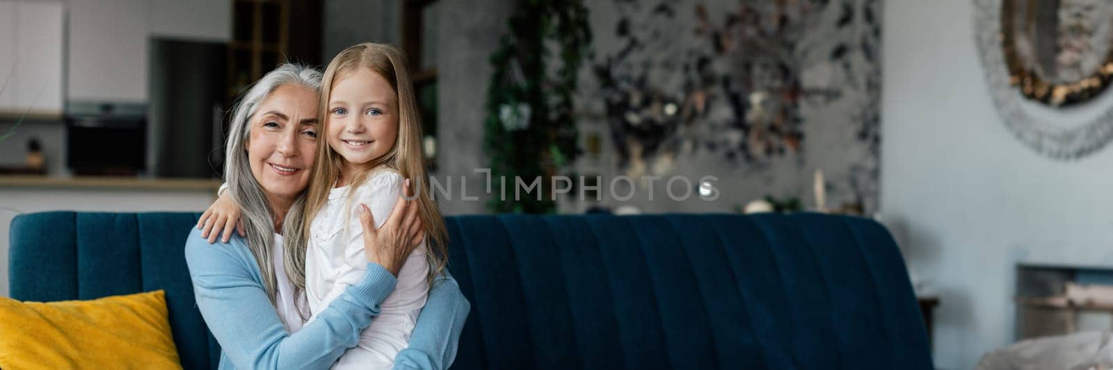 Love and family relationship. Happy european elderly grandmother and little granddaughter hugging, enjoying free time together in living room interior. People emotions, lifestyle at home, copy space
