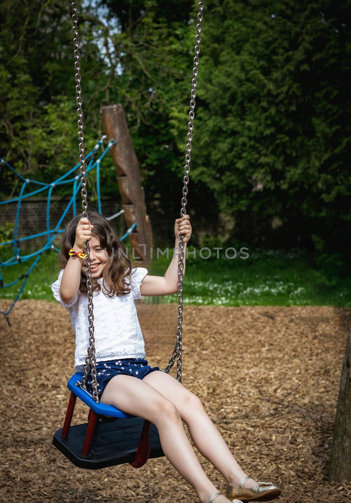 Portrait of one beautiful Caucasian brunette girl with flowing hair with happy emotions and a smile on her face, having fun and carefree riding on a swing on a summer day in the park on the playground, close-up side view.