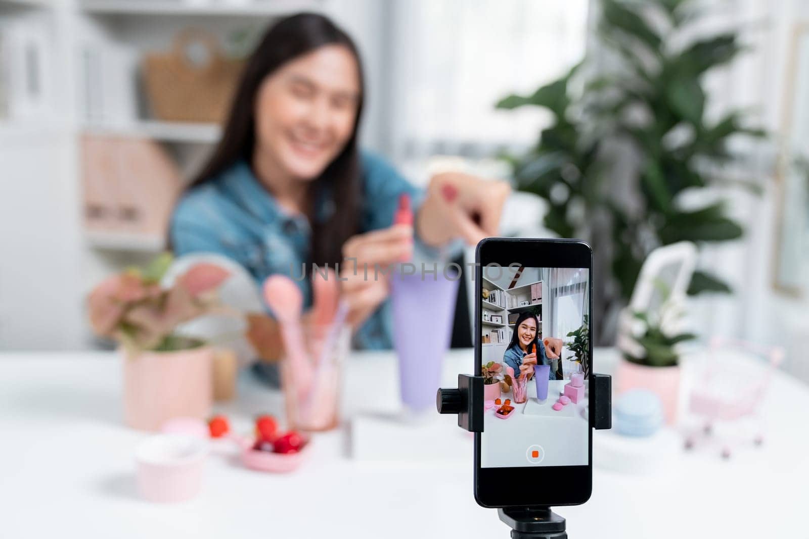 Selective focus phone with young beautiful Asian showing cosmetic makeup lipstick matte pastel color testing bestseller collection on arm test promotion on social media online recording. Stratagem.