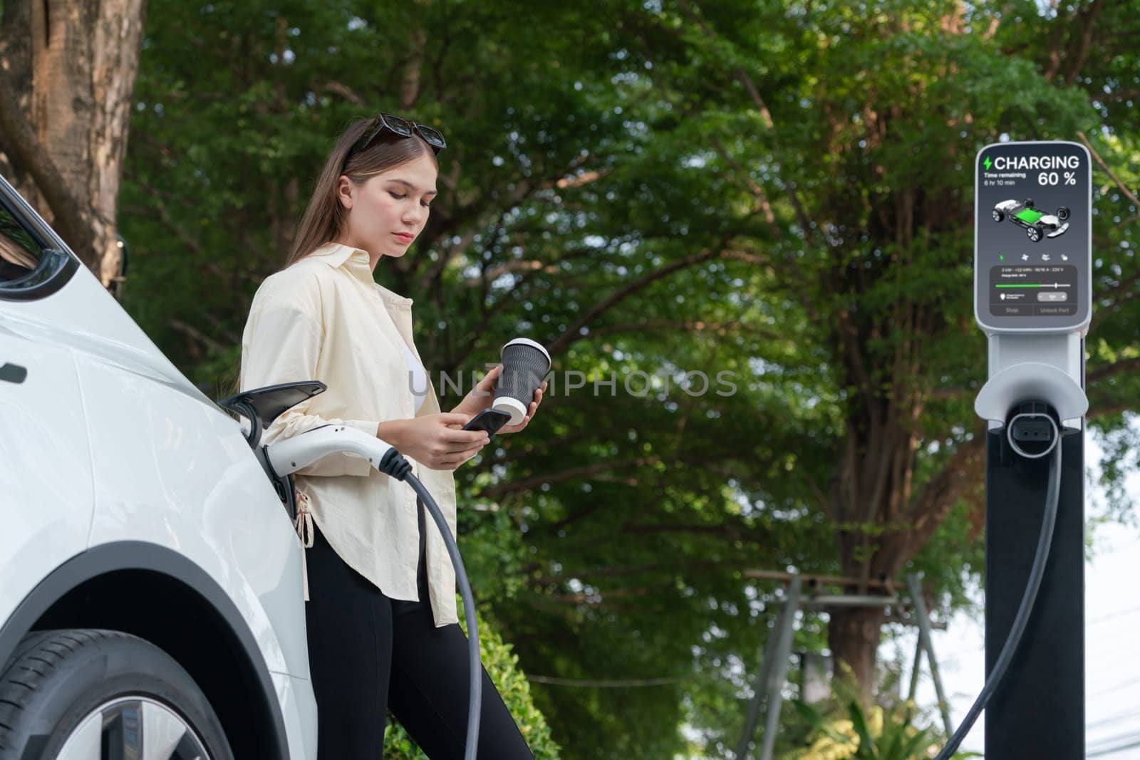 Young woman with coffee cup and sustainable urban commute with EV electric car recharging at outdoor cafe in springtime garden, green city sustainability and environmental friendly EV car. Expedient