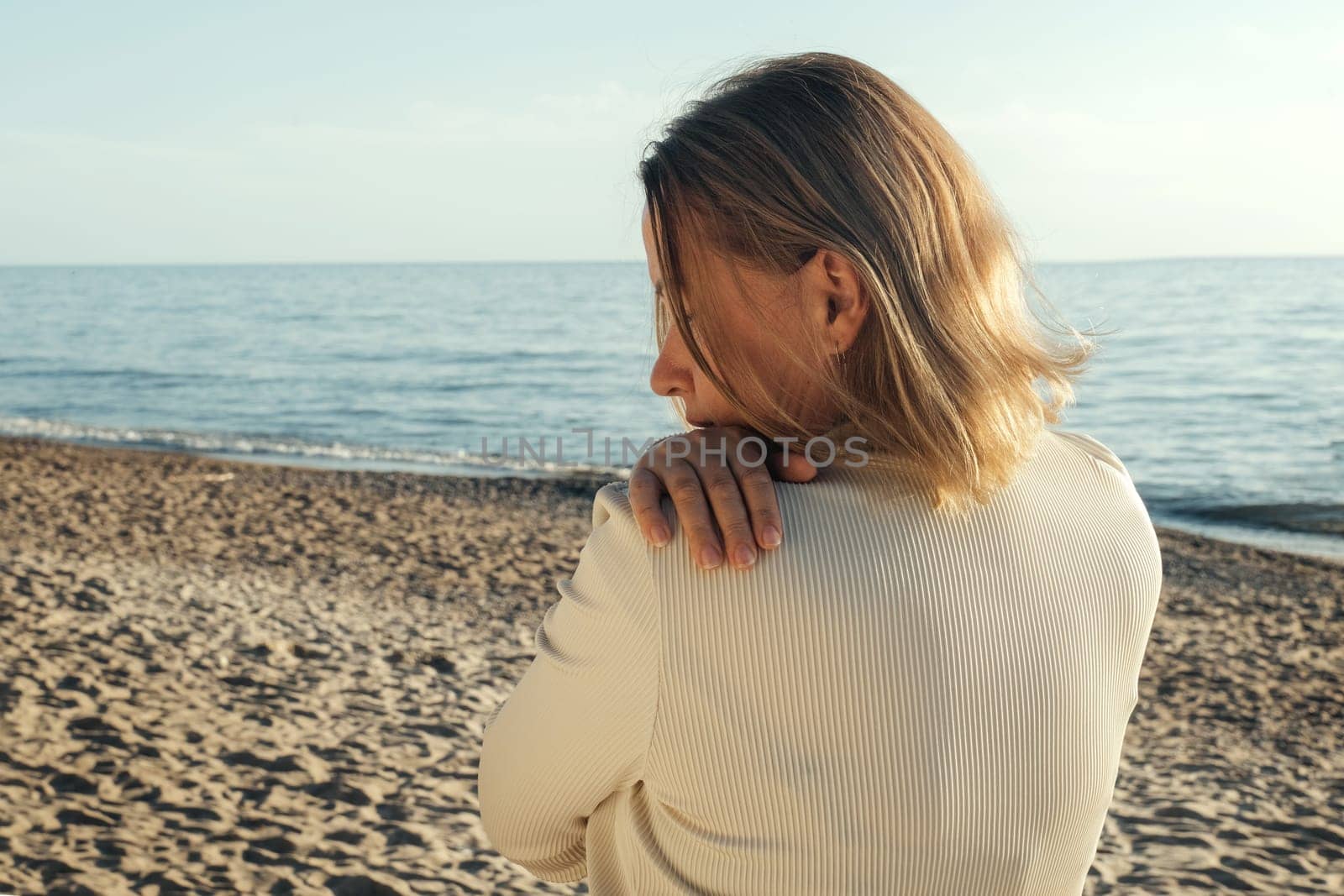 A woman standing on a sandy beach next to the ocean, looking out at the waves.