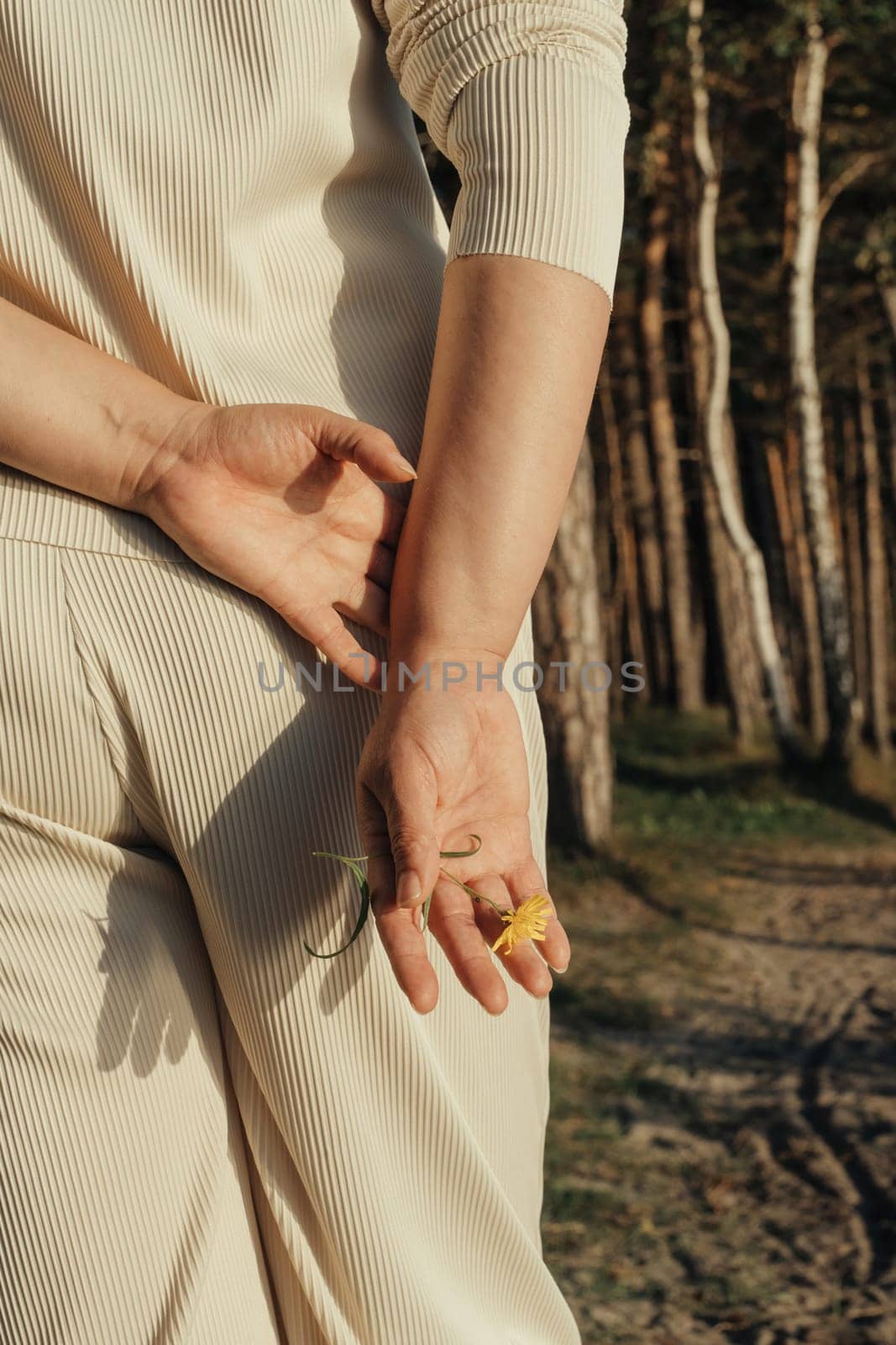 A woman holds her hands behind her back, against the background of a forest.