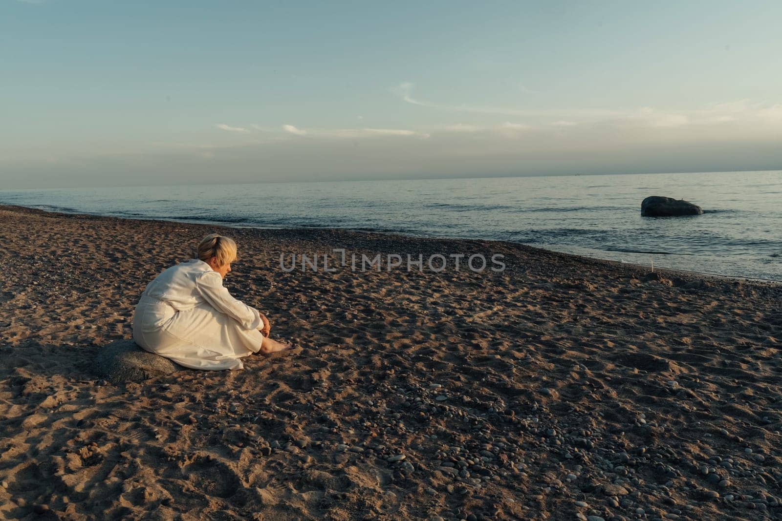 A woman sits on the sandy beach next to the vast ocean, enjoying the view and peaceful sound of the waves.