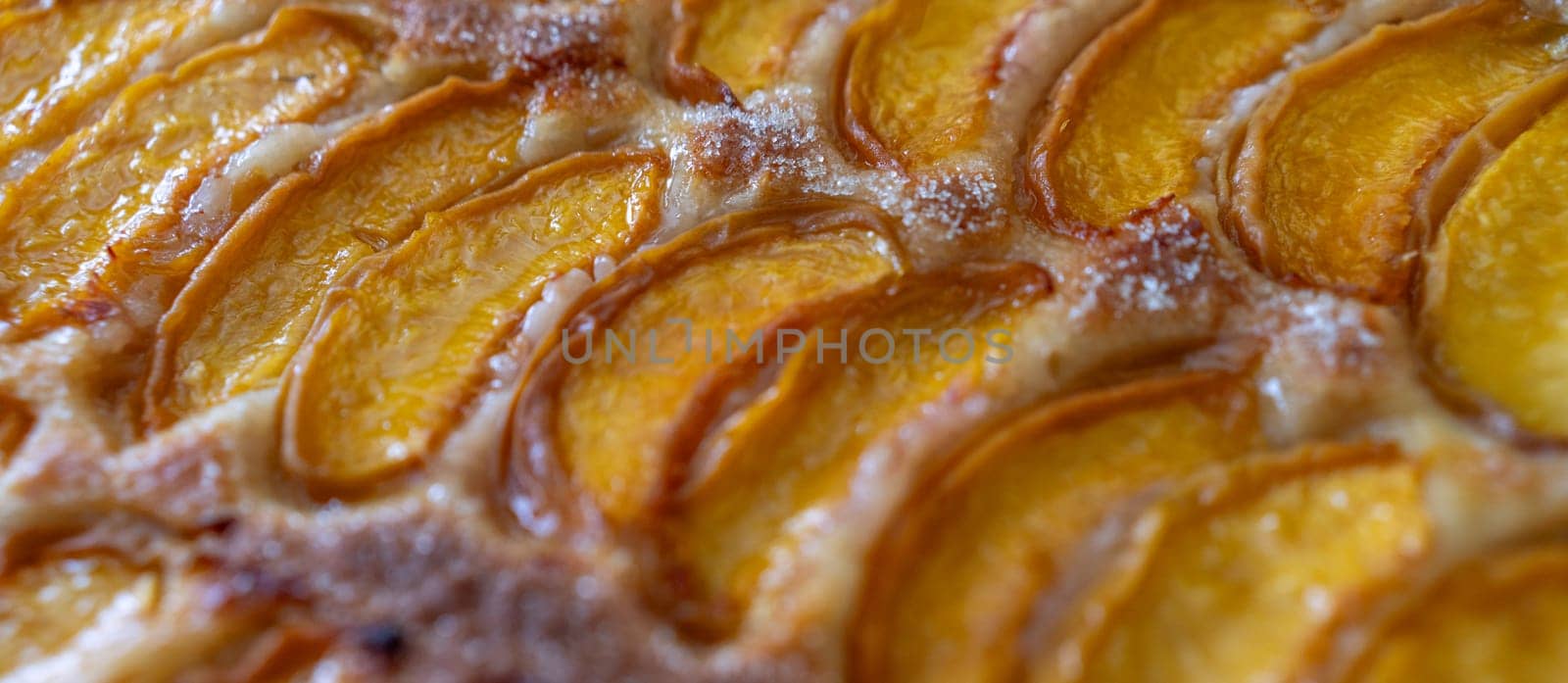 A close up of a dessert made of sliced peach. The dessert is covered in a caramel glaze and has a golden brown crust. The peach are arranged in a spiral pattern, creating a visually appealing.