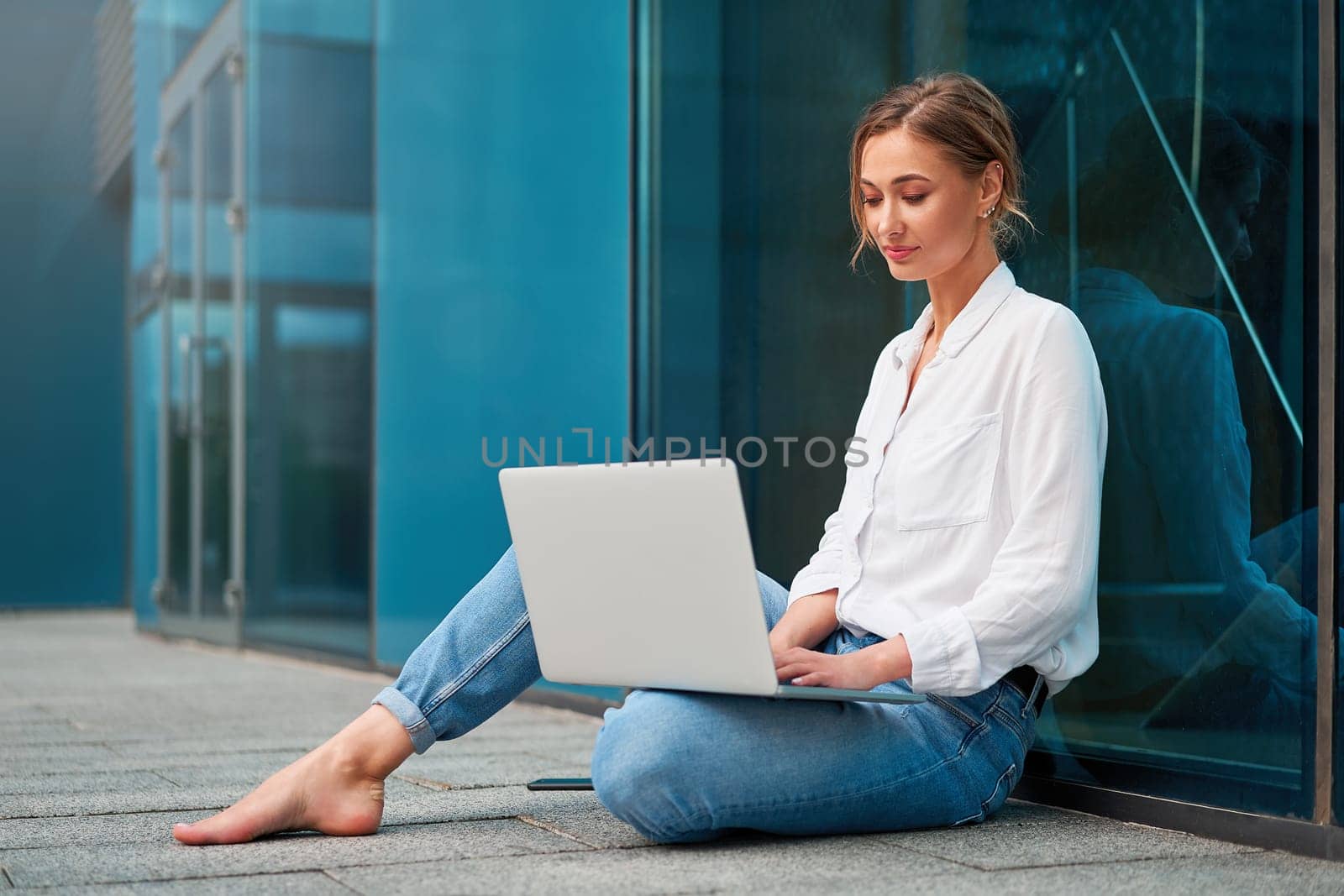 Young woman checking email on laptop sitting on the ground outside by andreonegin