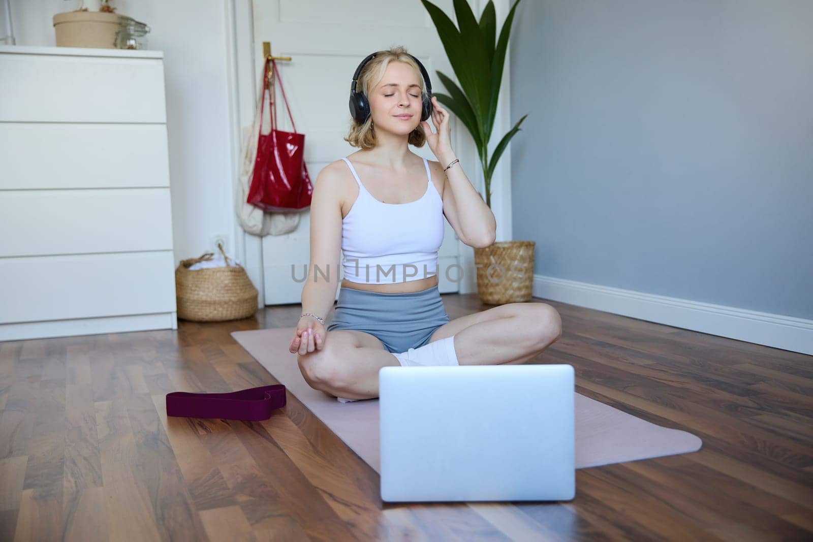 Portrait of fit and healthy woman at home, practice yoga, sitting on rubber mat, listening to instructions online, using meditation music to relax, following guidance on laptop.