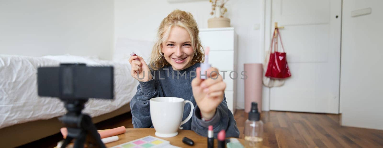 Lifestyle, beauty blogger, woman recording video of her putting on makeup, talking to camera, making online tutorial, showing her lip gloss or lipstick to followers, sitting on floor with cup of tea by Benzoix