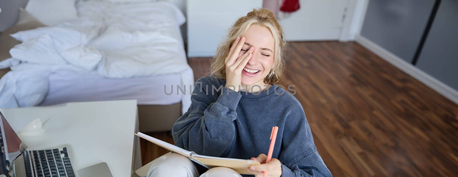 Portrait of charismatic blond girl, smiling woman in bedroom, holding notebook and pen, writing in journal or diary, creates to do list in planner.