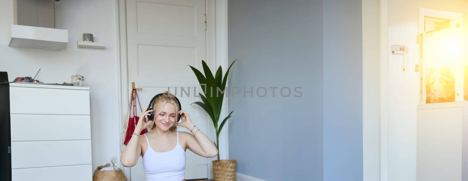 Portrait of young woman at home, connects to online gym training session, following fitness instructions on laptop, wearing wireless headphones during workout.