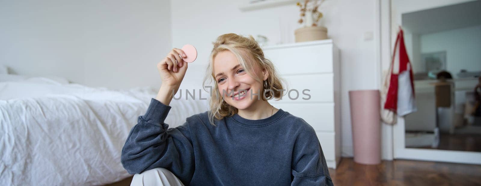 Portrait of beautiful and stylish young woman, vlogger recording video on her digital camera in a room, showing beauty products, making makeup tutorial for followers on social media.