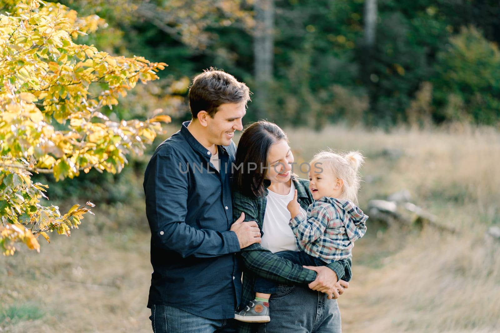 Smiling mom and dad holding little girl in their arms looking at her. High quality photo