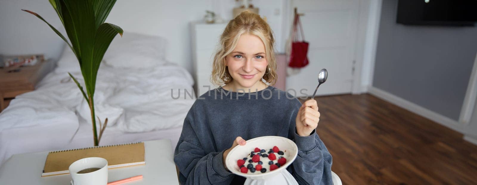 Portrait of young vlogger, content creator, showing her homemade breakfast on camera, eating dessert, smiling and looking happy.