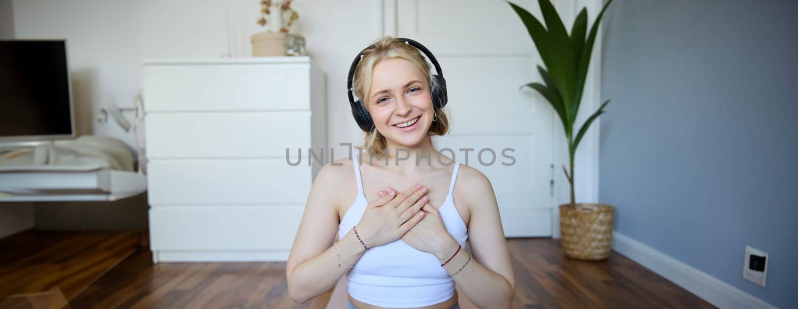 Portrait of young happy woman in headphones, looking with relaxed, friendly face expression, holding hands on her chest and smiling.