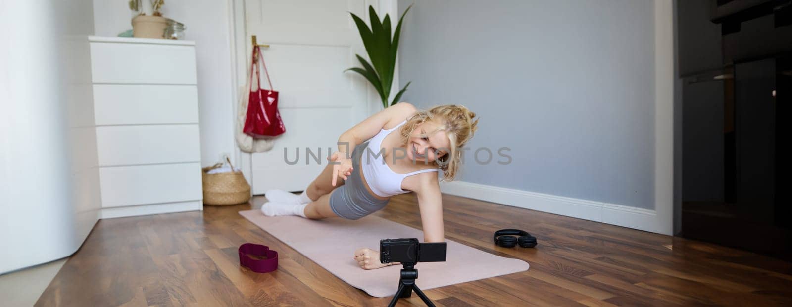 Portrait of fit and healthy young vlogger, fitness instructor woman standing in side plank, recording online lesson for clients on digital camera, shooting video about workout.