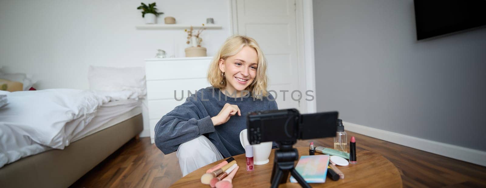 Portrait of young beautiful woman, lifestyle blogger, talking about makeup on camera, recording vlog, reviews product for social media account, vlogger working in her room.