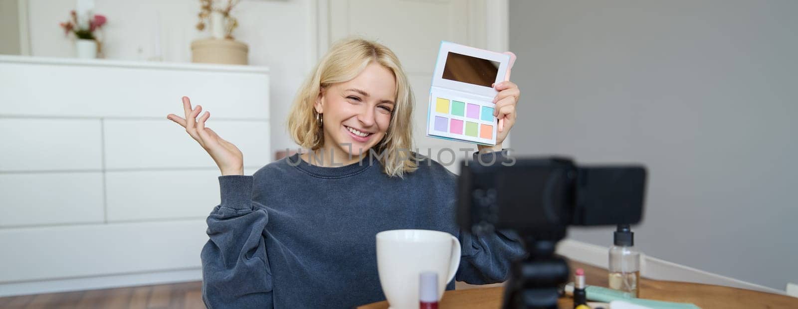 Lifestyle blogger, records video in her room, has a camera on coffee table, shows eyeshadow palette to her followers, does makeup tutorial, vlogger working indoors, creates content for social media by Benzoix