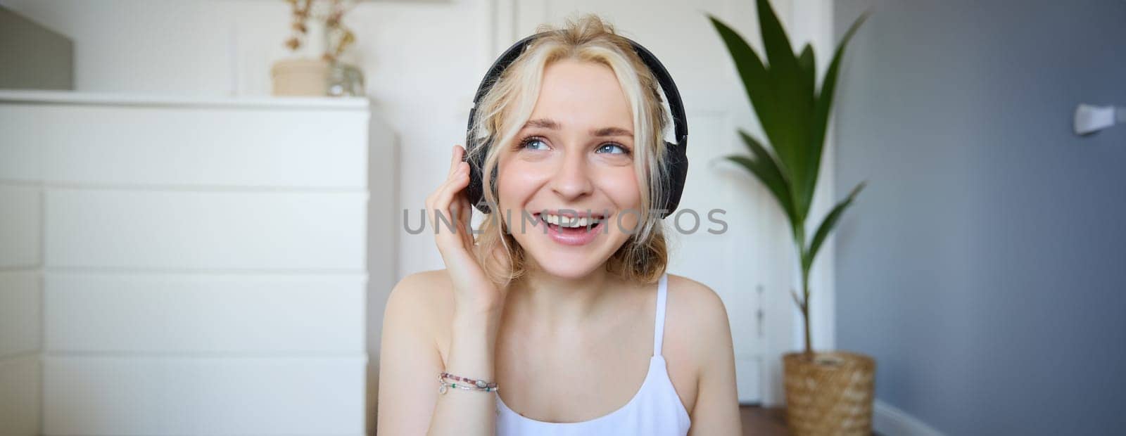 Portrait of happy and carefree blond woman, listens to music in wireless headphones, dancing and singing along favourite song, spending time alone at home.