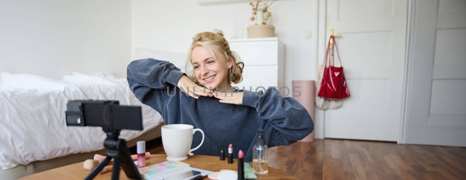 Lifestyle blogger records video of herself while doing hairstyle, showing makeup lifehacks for social media followers, vlogging, using camera for her blog, sitting in a room, drinking tea by Benzoix