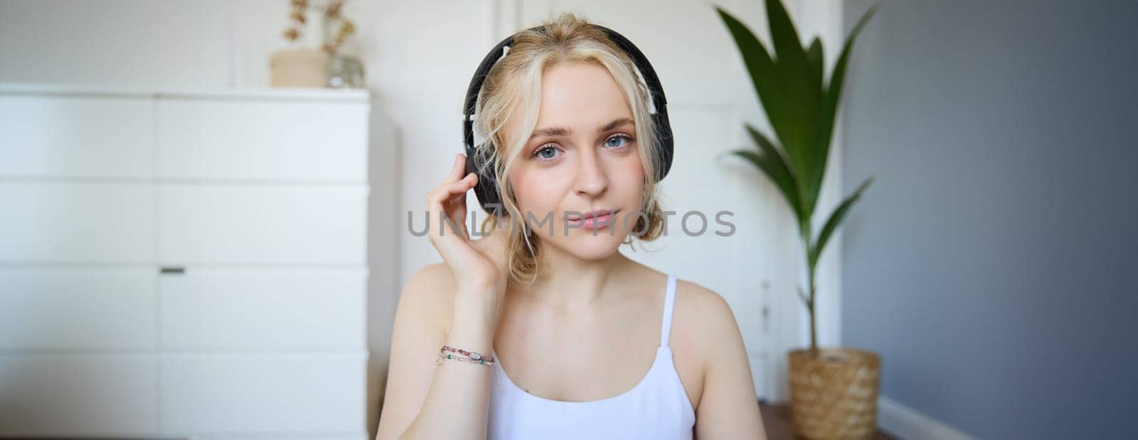 Portrait of happy and carefree blond woman, listens to music in wireless headphones, dancing and singing along favourite song, spending time alone at home.