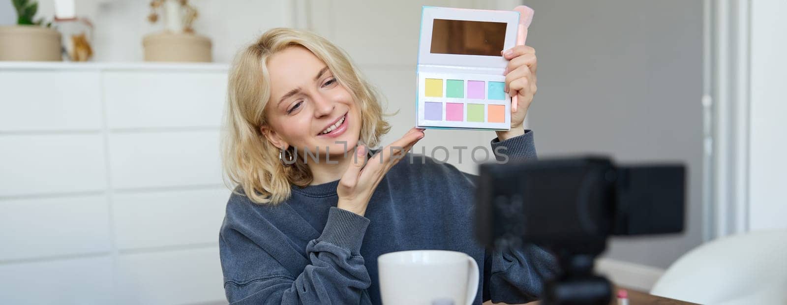 Portrait of beautiful lifestyle blogger, girl records a video on her camera for social media, shows palette of eyeshadows, does a makeup tutorial for her followers, sits in her room by Benzoix