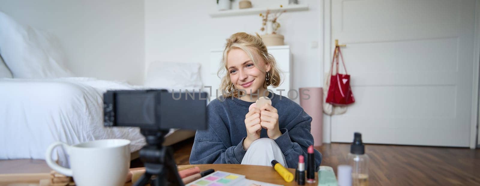 Portrait of beautiful and stylish young woman, vlogger recording video on her digital camera in a room, showing beauty products, making makeup tutorial for followers on social media by Benzoix