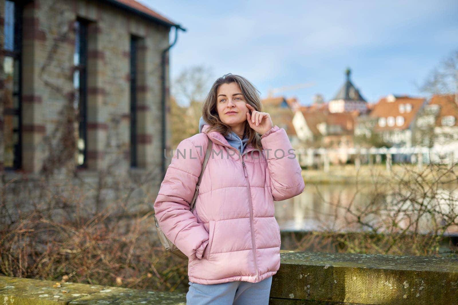 Young beautiful pretty tourist girl in warm hat and coat with backpack walking at cold autumn in Europe city enjoying her travel in Zurich Switzerland. Outdoor portrait of young tourist woman enjoying sightseeing