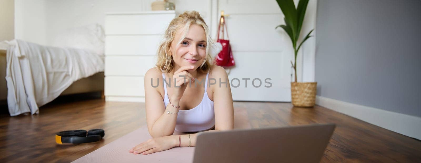 Portrait of young fitness woman, doing workout at home, looking at her gym instructor on laptop screen, doing online training session.